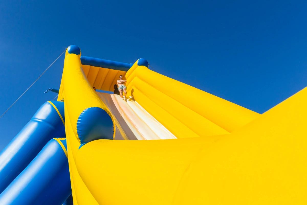 oung man caucasian exciting thrill ride down high water slide inflated amusement structure on beach summer holidays.